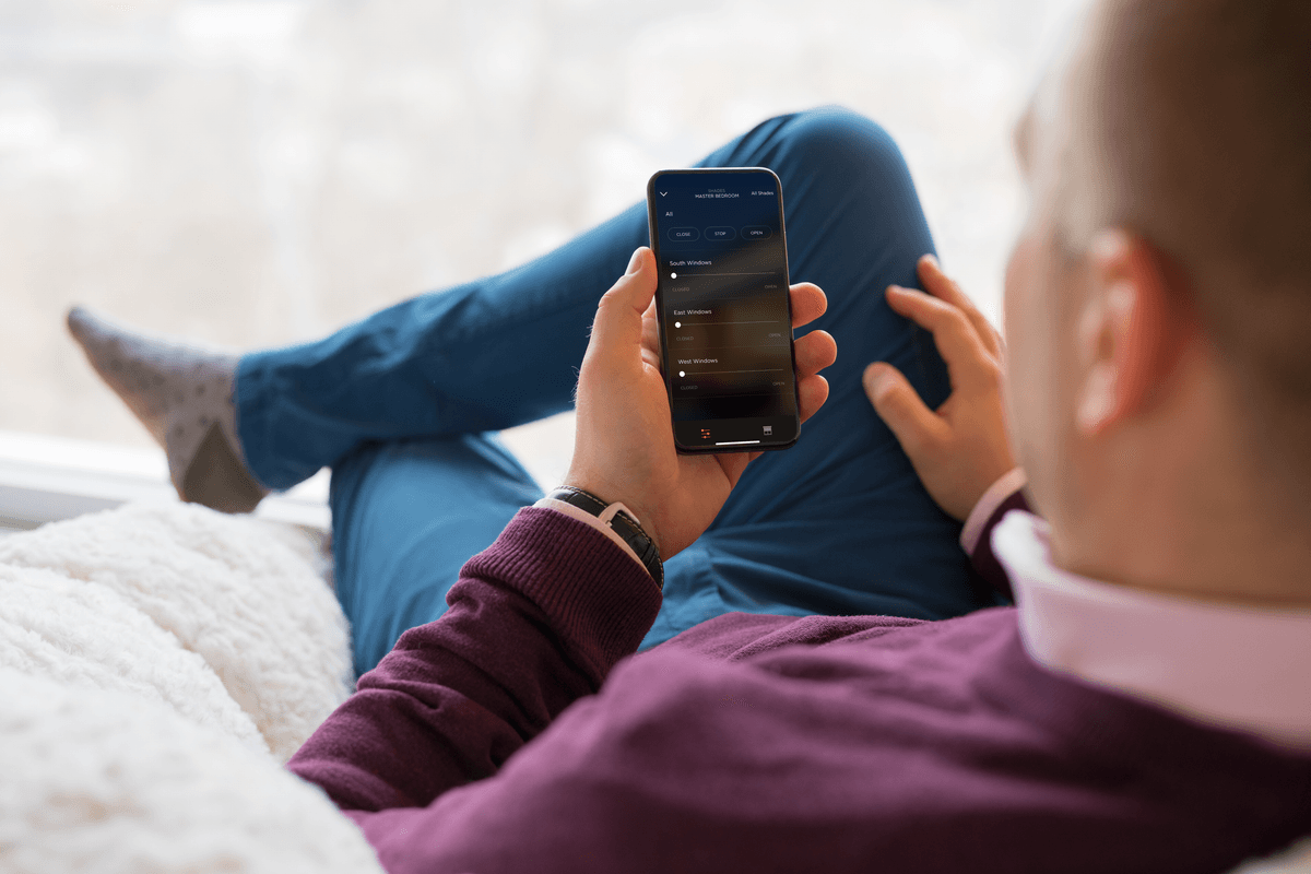 Man using Savant app on iPhone to control motorized shades